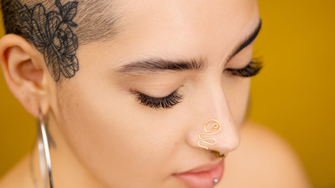 Close-up of a woman with a nose ring and minimal makeup against a yellow background wearing volume lash extensions.