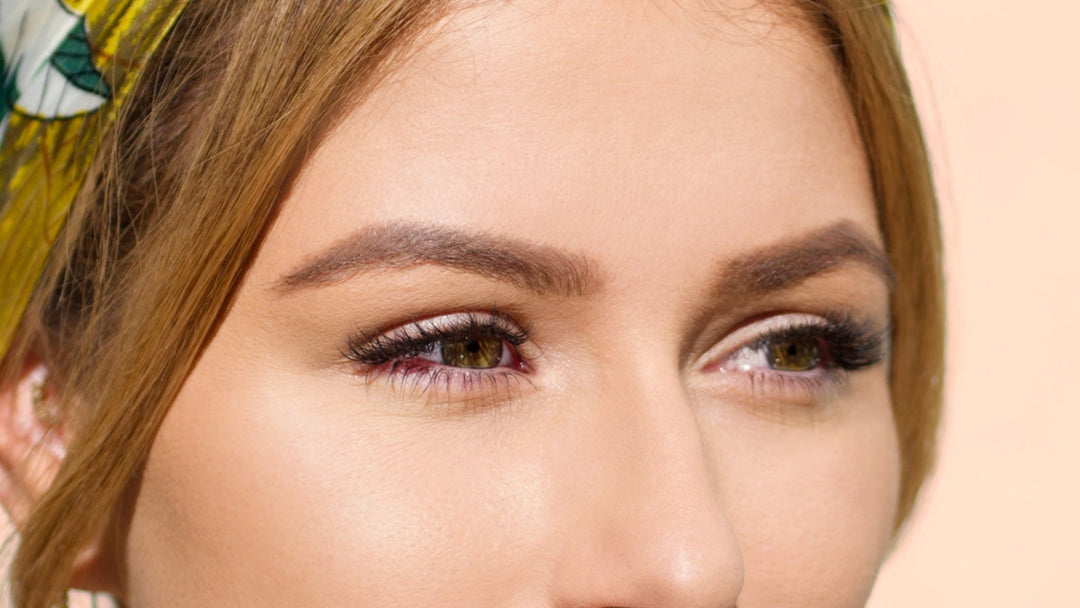 Woman wearing a patterned headscarf on a peach background wearing hybrid lash extensions.  A mix of volume and classic lashing techniques.