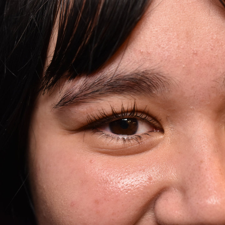 Close-up of a person's face with dark hair and brown eyes with a straight on view of on eye after a lash lift.