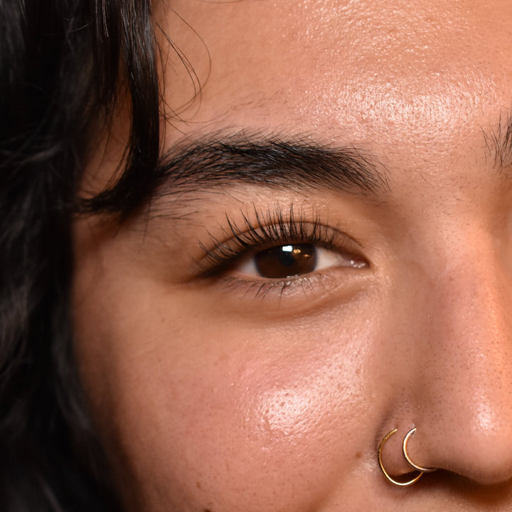 Close-up of a person with dark hair and a nose ring against a neutral background with a single eye close up after a lash lift.