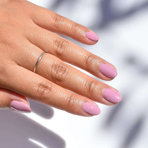 A close up of a mid toned hand coming in the upper left hand corner with one silver ring on. The nails art painted with Owl You Need is Love nail polish from Hello Birdie which is a light taupe purple hue. The white background has soft shadows of leaves.