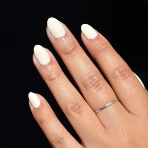 A close up of the four fingers of a mid toned hand comes from the lower right hand corner, brightly illuminated with the background in black shadow. The nails are painted with Three Little Birdies nail polish from Hello Birdie which is a light pastel yellow hue. The middle finger has a thin silver ring.